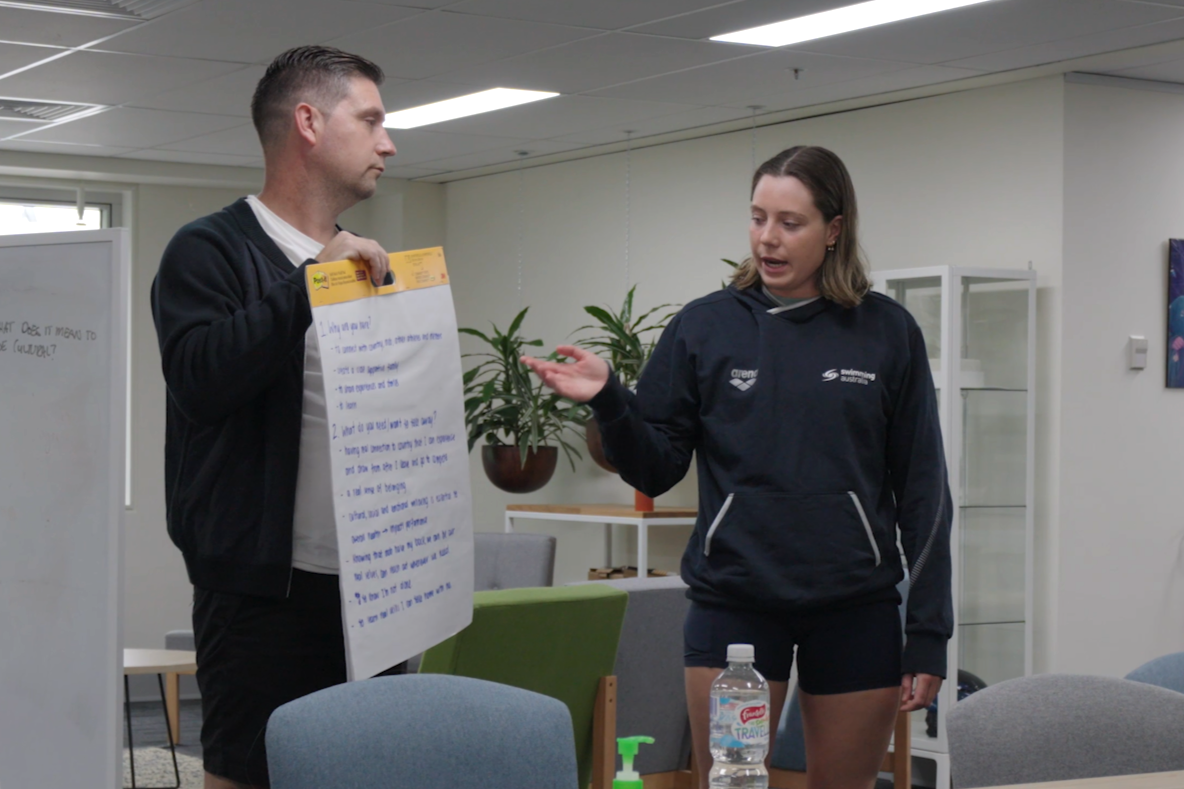 Ben Austin holds post-it note while Bianca points and talks.