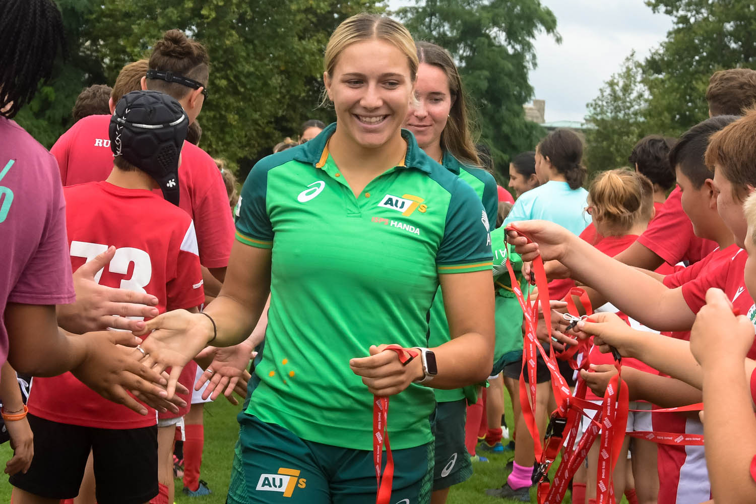 A rugby 7s player receives a medal from children while running through a group.