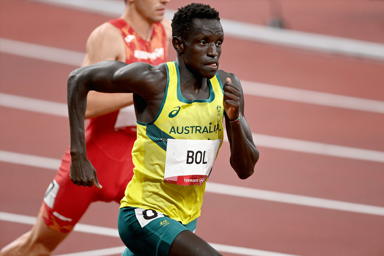 Australian 800m runner Peter Bol running at the Tokyo Olympic Stadium, wearing Australia's green and gold athletics uniform.