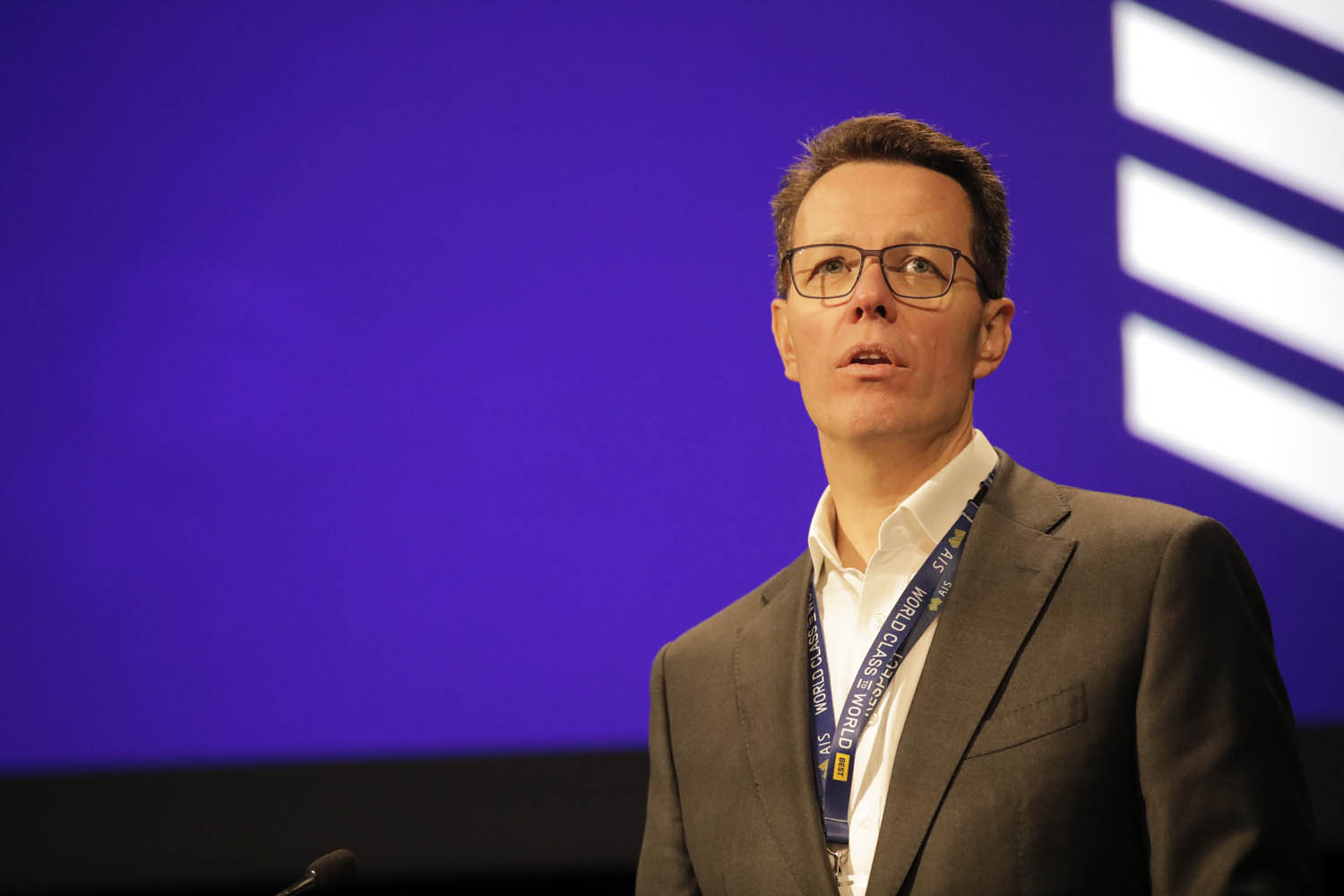 Kieren Perkins behind a lectern, in front of a blue screen.