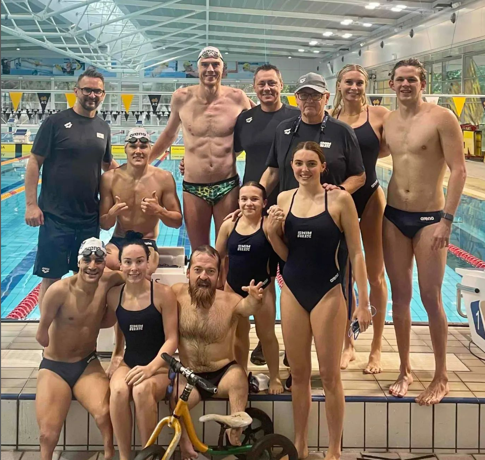 Para swimmers sitting and standing on edge of pool smiling.