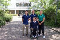 Three athletes standing and one athlete in a wheelchair gathered outside at the AIS.
