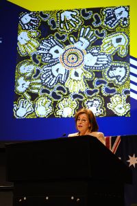 Josephine Sukkar stands beneath an Aboriginal artwork projected onto the wall behind her.