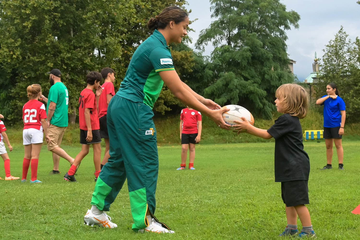 A rugby 7s player hands a ball to a child