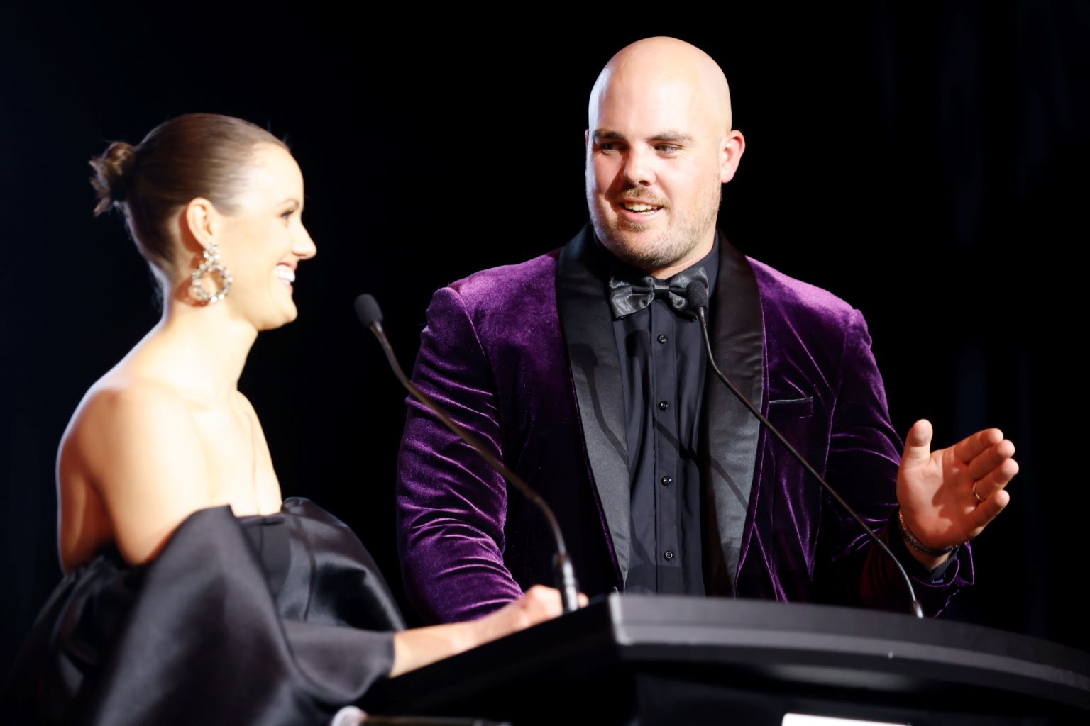 Two people stand on stage smiling in formal dress.