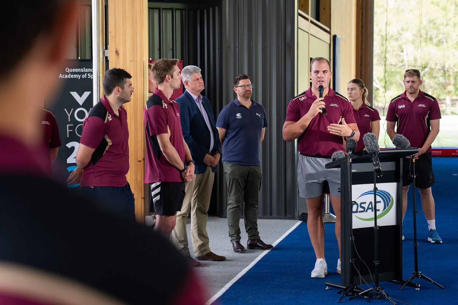 A group of people gathered wearing Queensland Academy of Sport shirts