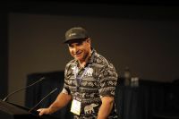 A man stands behind microphones, smiling.