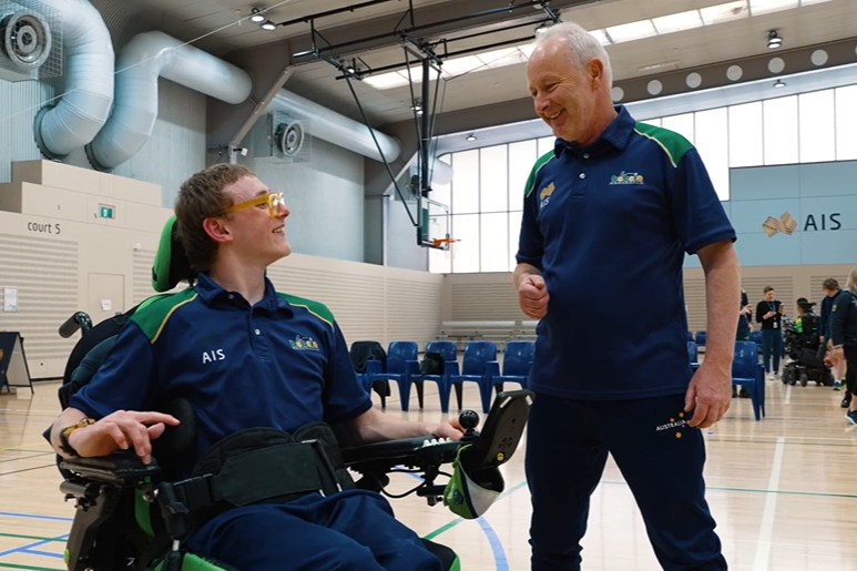 Dylan in wheelchair smiles up at his coach.