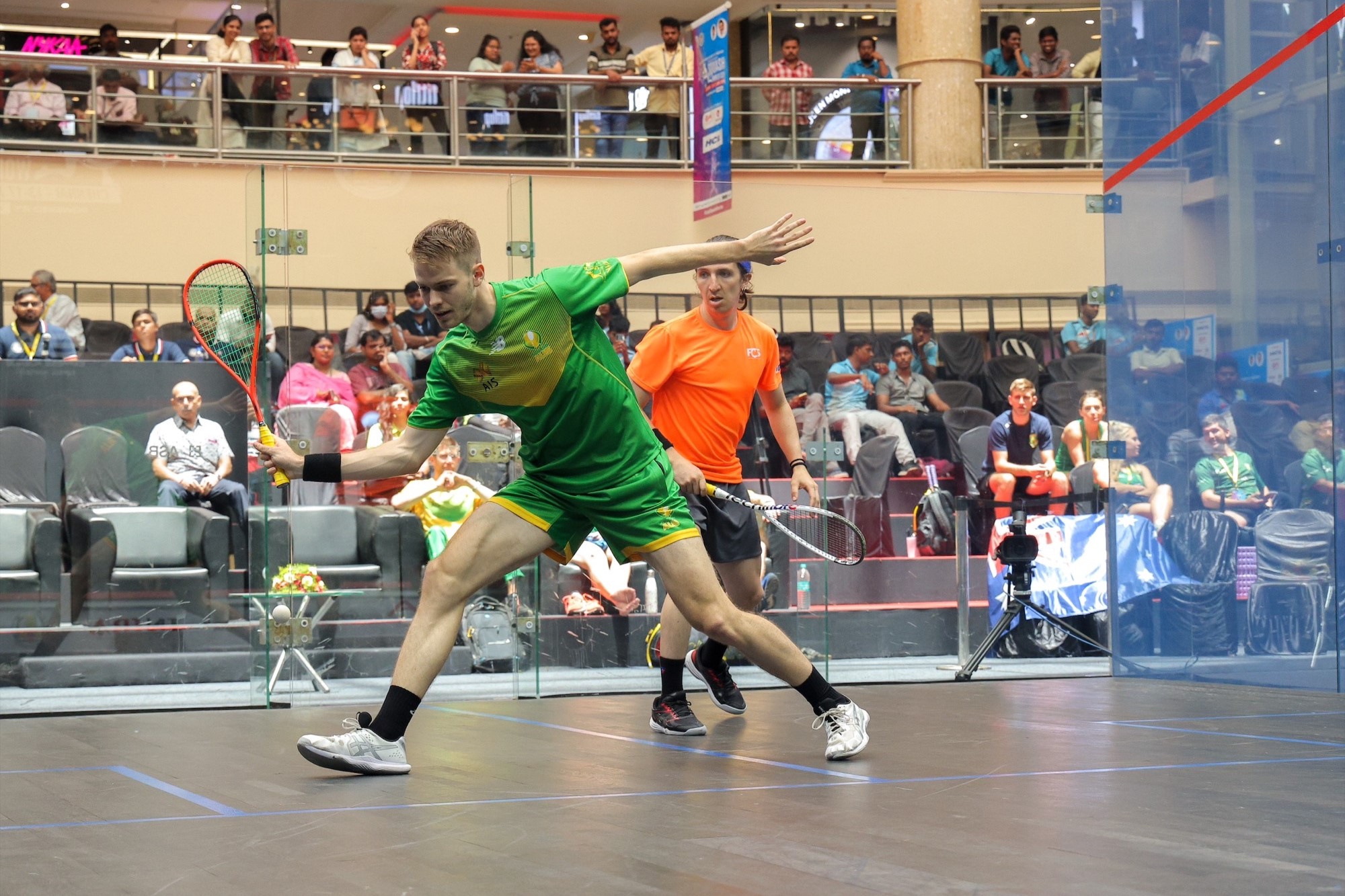 Jo White swings at squash ball, with opponent and crowd watching on.