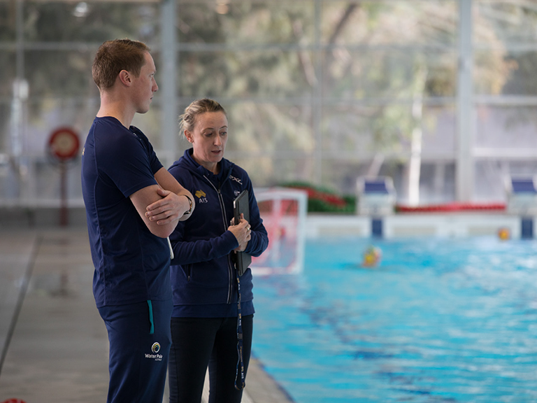 Two coaches standing by a pool