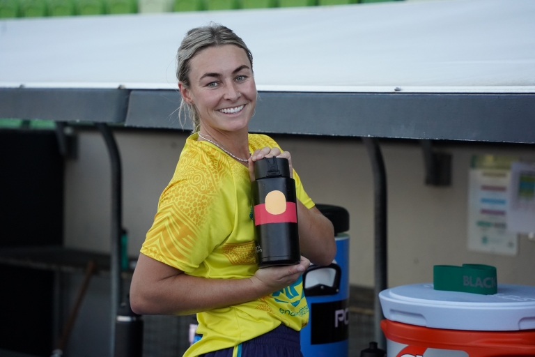 Mariah Williams smiling holding black drink bottle with Indigenous flag on it.