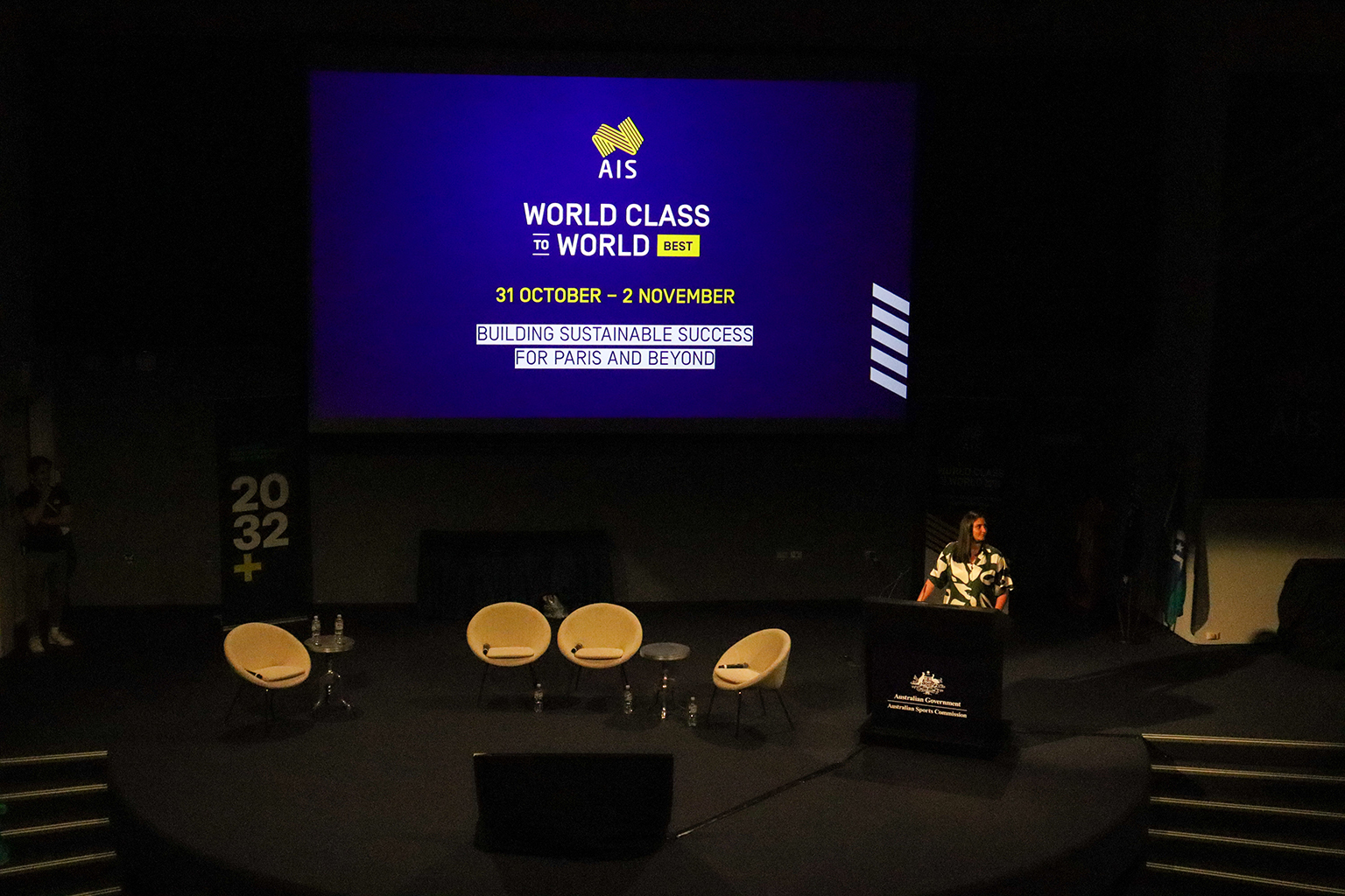 A dark stage with a woman standing behind a lectern